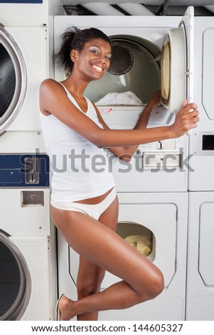 Portrait of happy young woman standing by dryer in laundry