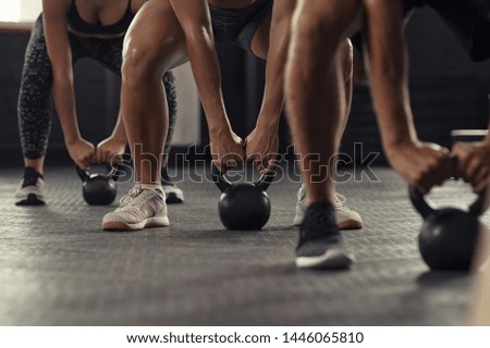 Closeup of young man and fit woman hands lifting kettle bell while squatting at gym. Athlete people doing weight lifting with kettlebell. Group of three young athlete doing crossfit training. Royalty-Free Stock Photo #1446065810