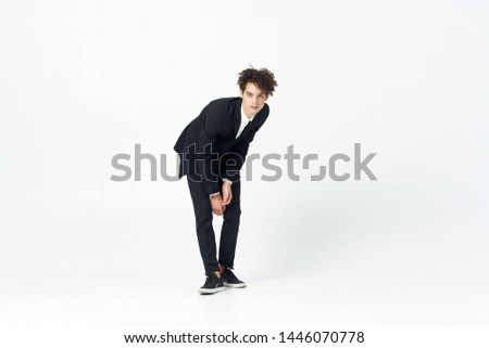 A guy with curly hair and a suit bent forward on a bright isolated background in full growth                     