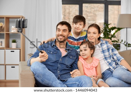 family, technology and people concept - happy father, mother, little son and daughter taking picture by smartphone on selfie stick at home