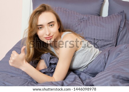 Beautiful girl lying on the bed in the morning and shows a hand  like sign : good sleep concept.