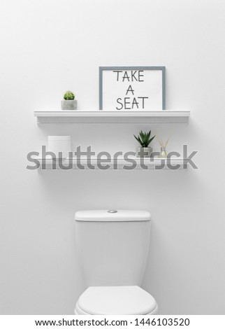 Toilet bowl, decor elements and funny sign near white wall. Bathroom interior