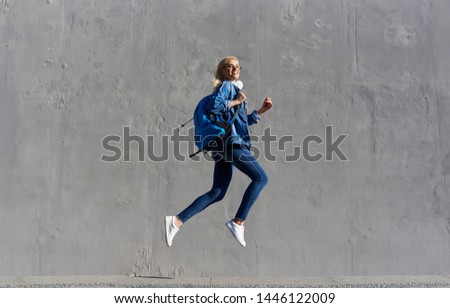 Full body Portrait of happy young woman walking with bag and cellphone. Cheerful student  running in air over gray background