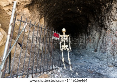 Skeleton in the mouth of a mine by No Trespassing sign in the desert
