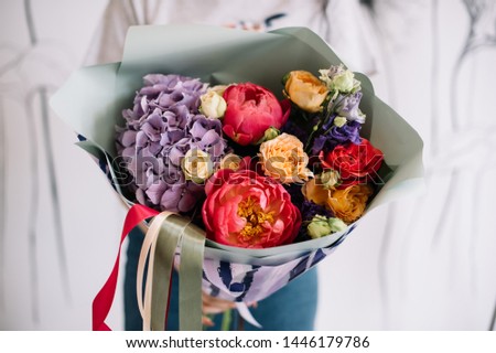 Very nice young woman holding big and beautiful bouquet of fresh hydrangea, roses, peony, eustoma in red, orange and purple colors, cropped photo, bouquet close up