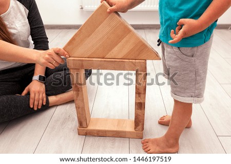 The son and mother is playing in the room and build the house from wooden blocks