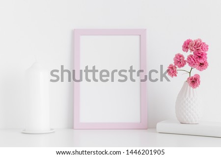 Pink frame mockup with pink roses in a vase and candle on a white table.Portrait orientation.