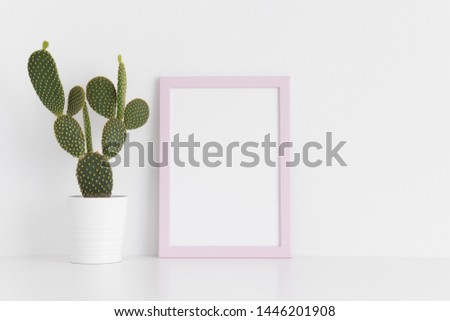 Pink frame mockup with a opuntia cactus in a pot on a white table. Portrait orientation.