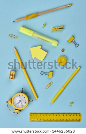 Yellow stationery supplies on blue background. Yellow alarm clock and various school items. Flat lay, top view.