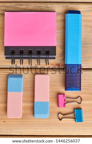 School supplies on wooden background. Spiral notepad, marker, paper clamps and erasers. Flat lay, top view.