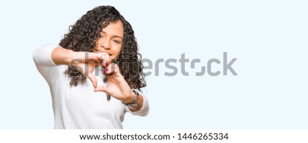 Young beautiful woman with curly hair wearing turtleneck sweater smiling in love showing heart symbol and shape with hands. Romantic concept.