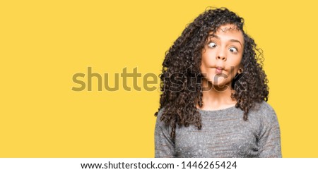 Young beautiful woman with curly hair wearing grey sweater making fish face with lips, crazy and comical gesture. Funny expression.