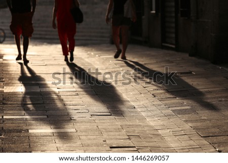 Outdoor urban view from back of people walking in a street. Long dark shadows drawn on a french sidewalk with people's legs and feet. Abstract picture of silhouettes lighted by the sun in the evening.