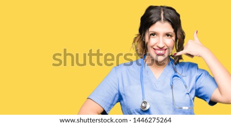 Young adult doctor woman wearing medical uniform smiling doing phone gesture with hand and fingers like talking on the telephone. Communicating concepts.