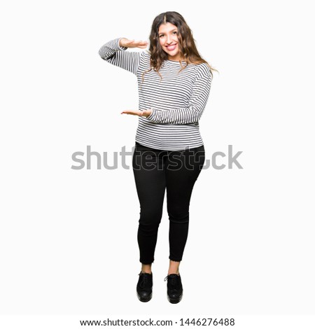 Young beautiful woman wearing stripes sweater gesturing with hands showing big and large size sign, measure symbol. Smiling looking at the camera. Measuring concept.