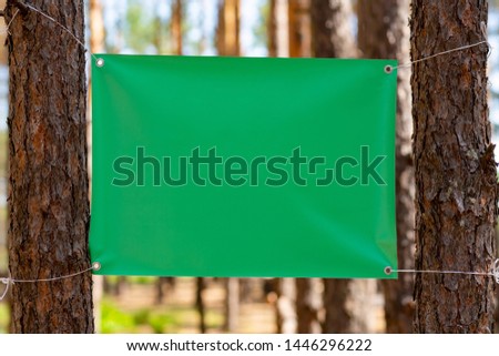 Blank green canvas with copy space for your text message or content for advertising stretched between two trees/Empty vinyl canvas on the blurred background outdoor
