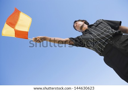 Low angle view of a soccer linesman waving flag against clear blue sky