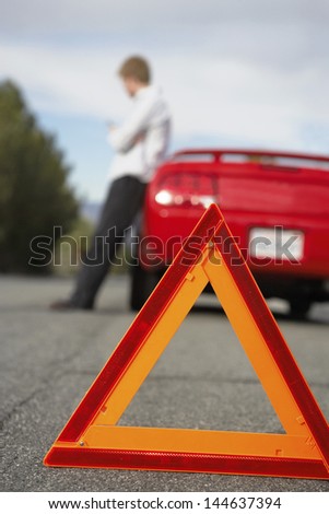 Emergency stop sign in foreground with blurred man leaning by broken down car