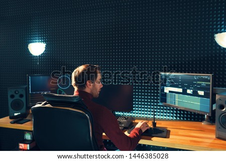 Video editing. Professional editor adding special sound effects. Back view of young man watching graphs on monitors. Copy space on gray wall