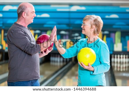 Smiling mature couple holding bowling ball giving high-five
