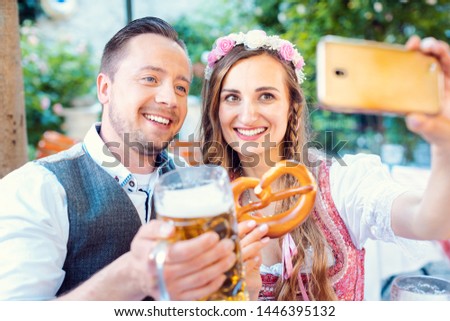 Cheerful couple in German beer garden taking a selfie picture with the phone