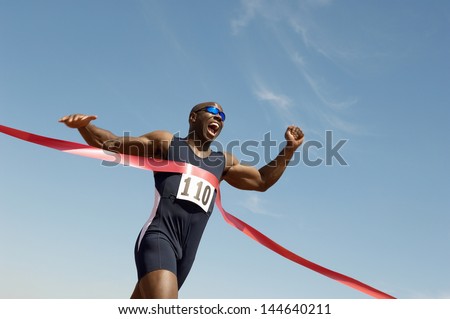 Low angle view of an African American male runner winning race against blue sky Royalty-Free Stock Photo #144640211