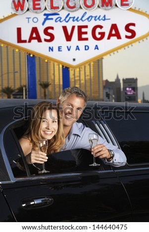 Happy couple in limousine with champagne flutes in front of welcome to Las Vegas sign