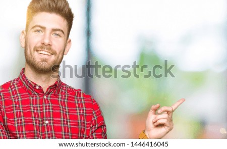 Young handsome man with a big smile on face, pointing with hand and finger to the side looking at the camera.