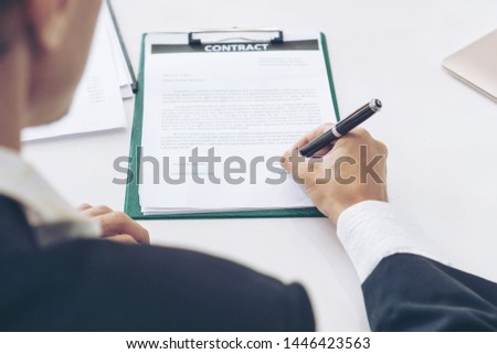 Image view cross shoulder to seeing young businessman handle a pen to sign in contract paper on table, copy space, business concept