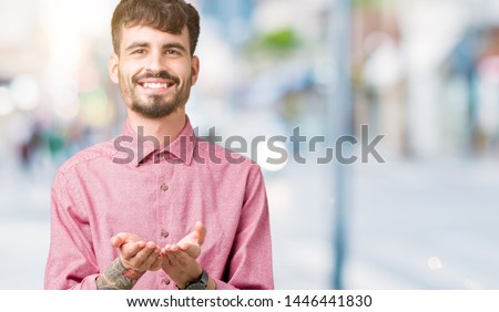Young handsome man wearing pink shirt over isolated background Smiling with hands palms together receiving or giving gesture. Hold and protection