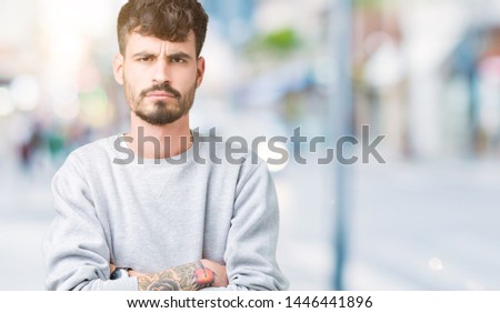 Young handsome man wearing sweatshirt over isolated background skeptic and nervous, disapproving expression on face with crossed arms. Negative person.