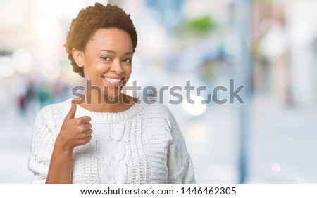 Beautiful young african american woman wearing sweater over isolated background doing happy thumbs up gesture with hand. Approving expression looking at the camera showing success.