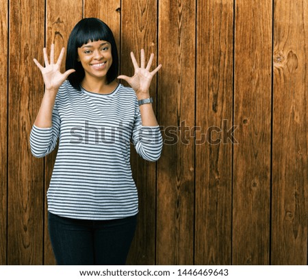 Beautiful young african american woman wearing stripes sweater over isolated background showing and pointing up with fingers number ten while smiling confident and happy.