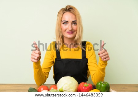 Young blonde woman with lots of vegetables giving a thumbs up gesture