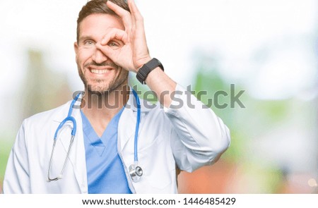 Handsome doctor man wearing medical uniform over isolated background doing ok gesture with hand smiling, eye looking through fingers with happy face.
