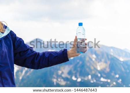 Female hand holding a plastic bottle with clear water on a green homa mountain background. Travel and thirst concept