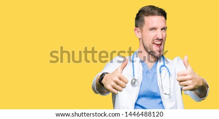 Handsome doctor man wearing medical uniform over isolated background approving doing positive gesture with hand, thumbs up smiling and happy for success. Looking at the camera, winner gesture.