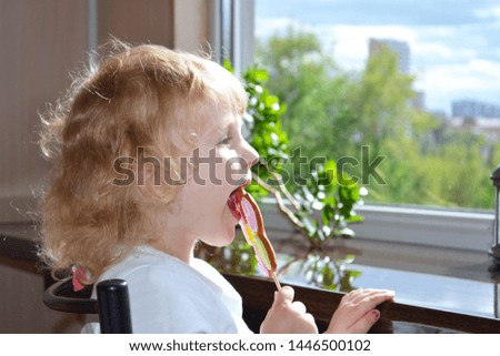 little cute girl eating cookies on a stick on the background of the window