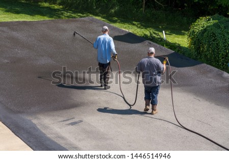 Workers applying blacktop sealer to asphalt street using a spray to provide a protective coat against the elements Royalty-Free Stock Photo #1446514946