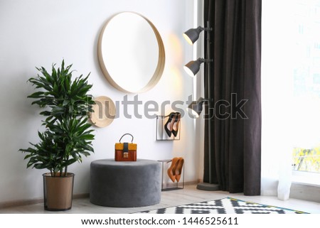Hallway interior with big round mirror and ottoman chair near white wall