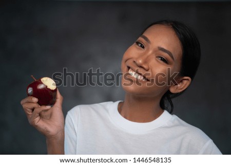 Portrait of beautiful young smiling woman in white t-shirt holding red apple over concrete background