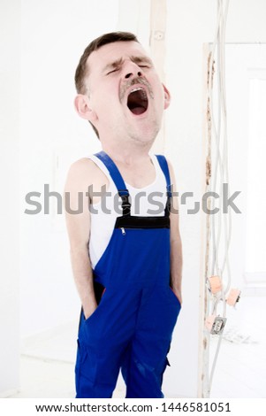 repairman with big head in a blue boilersuit is yawning