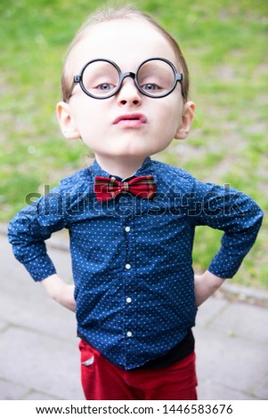 little boy with big head and glasses looking arrogant standing outdoors