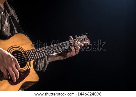 Guitarist, music. A young man plays an acoustic guitar on a black isolated background. Pointed light