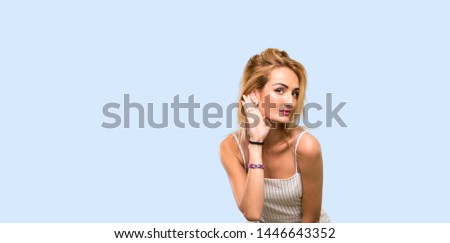 Young blonde woman listening to something by putting hand on the ear over isolated blue background