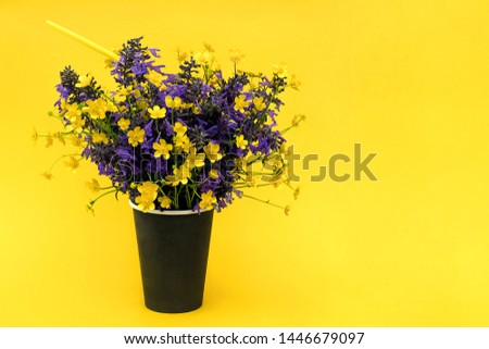 Bouquet of colored flowers in black paper coffee cup with cocktail straw on yellow background. Copy space Mockup Template for postcard, text, design Concept Hello summer or Taste of summer.