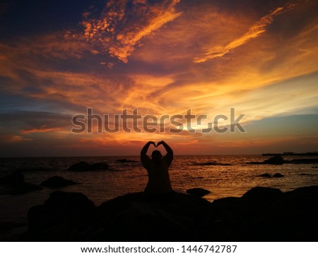 The girl shows the love symbol at the beach at dusk.