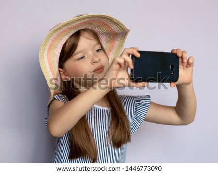 cute beautiful little girl in a dress and hat takes pictures, makes selfie with a smartphone