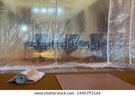 Plastic drop cloth hangs from ceiling to carpet floor to protect furniture from spills, paint drips and splatter, dust management, and debris during painting, demolishing or construction Royalty-Free Stock Photo #1446793166