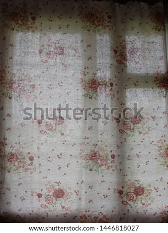 Dark wooden window frame silhouette shining through a floral print curtain on a sunny day